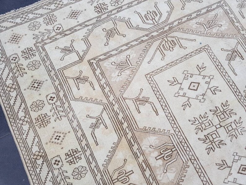 Puede incluir: Una alfombra beige con un patr&oacute;n geom&eacute;trico marr&oacute;n. El patr&oacute;n presenta motivos repetidos de flores estilizadas, estrellas y formas geom&eacute;tricas.