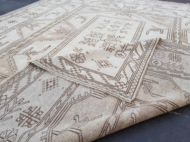 Puede incluir: Una alfombra de color blanco y marr&oacute;n con un dise&ntilde;o geom&eacute;trico. La alfombra est&aacute; doblada por la mitad, mostrando los intrincados detalles del patr&oacute;n tejido.