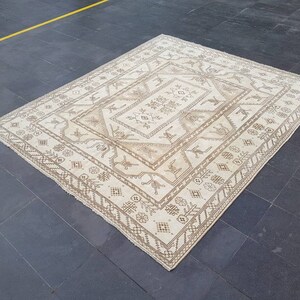 Puede incluir: Una alfombra blanca con un patr&oacute;n geom&eacute;trico marr&oacute;n. La alfombra tiene una forma de diamante central con formas de diamantes m&aacute;s peque&ntilde;as que la rodean.
