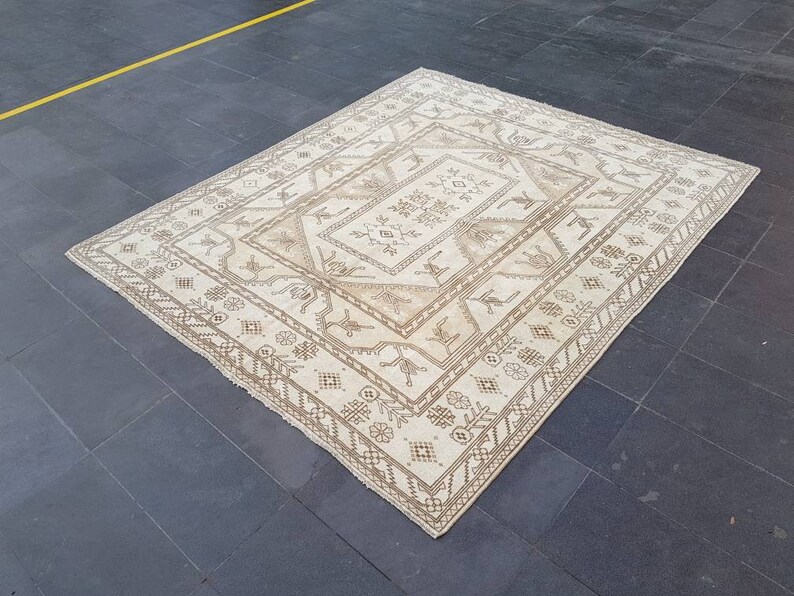 Puede incluir: Una alfombra blanca con un patr&oacute;n geom&eacute;trico marr&oacute;n. La alfombra tiene una forma de diamante central con formas de diamantes m&aacute;s peque&ntilde;as que la rodean.