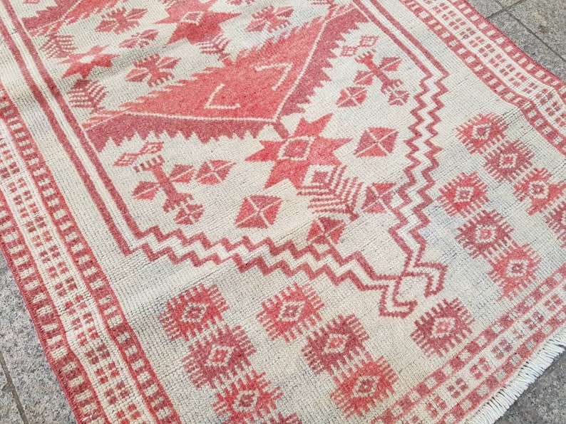 K&ouml;nnte beinhalten: Rechteckiger Teppich mit cremefarbenem Hintergrund und rotem geometrischen Muster. Das Design umfasst Diamanten, Kreuze und Zickzackformen. Der Teppich hat einen Fransenrand und misst ca. 152 cm lang und 91 cm breit.
