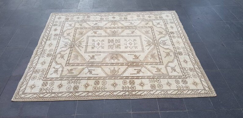 Puede incluir: Una alfombra de color crema con un patr&oacute;n geom&eacute;trico marr&oacute;n. La alfombra tiene un medall&oacute;n central con un patr&oacute;n repetitivo de flores y hojas estilizadas.