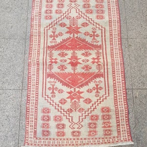 K&ouml;nnte beinhalten: Ein rechteckiger Teppich mit cremefarbenem Hintergrund und rotem geometrischem Muster. Der Teppich hat ein zentrales Design mit Diamanten und Sternen, das von einem roten Rand umrahmt wird. Der Teppich hat an den kurzen Enden einen Fransen.