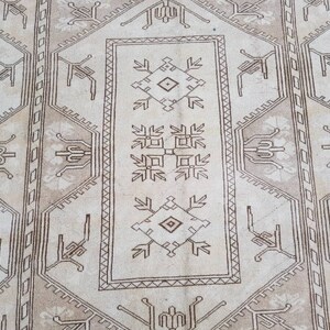 Puede incluir: Una alfombra beige con un patr&oacute;n geom&eacute;trico marr&oacute;n. El patr&oacute;n presenta motivos repetidos de flores y hojas estilizadas.