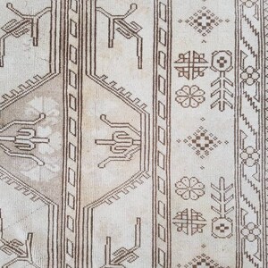 Puede incluir: Primer plano de una alfombra beige con un patr&oacute;n geom&eacute;trico marr&oacute;n. El patr&oacute;n presenta dise&ntilde;os repetidos de flores estilizadas, hojas y formas geom&eacute;tricas.