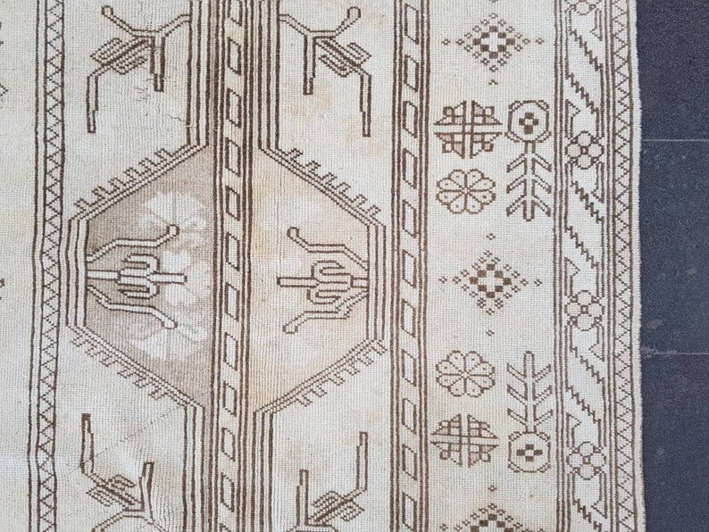 Puede incluir: Primer plano de una alfombra beige con un patr&oacute;n geom&eacute;trico marr&oacute;n. El patr&oacute;n presenta dise&ntilde;os repetidos de flores estilizadas, hojas y formas geom&eacute;tricas.