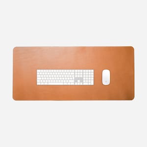 May include: A rectangular tan leather desk mat featuring a smooth surface. Centered on the mat is a white wireless keyboard with a numeric keypad, and to the right of the keyboard sits a white wireless computer mouse on the leather surface.