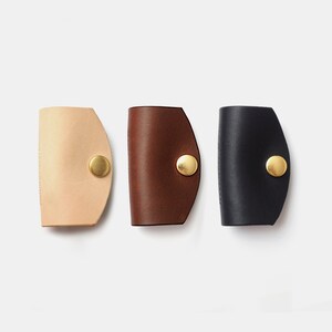 May include: Three leather keychains in different colors: beige, brown, and black. Each keychain has a gold metal button.