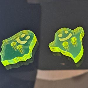 May include: Two bright yellow plastic ghost-shaped ornaments with a smiling face and two small holes.