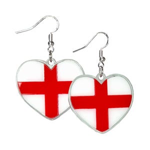 May include: A pair of heart-shaped earrings displaying the flag of England. Each earring has a white background with a red cross, and a silver-coloured hook. A patriotic accessory.
