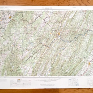 Puede incluir: Un mapa vintage de Cumberland, Tennessee, impreso en un fondo de papel blanco. El mapa muestra la topografía del área con líneas verdes, marrones y azules. El mapa está titulado "CUMBERLAND" en la parte superior central. El mapa está rodeado por un borde blanco.