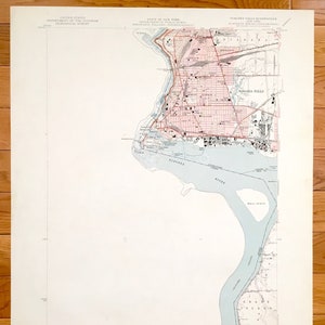 Pode incluir: Um mapa vintage de Niagara Falls, Nova Iorque, impresso em papel cor de creme. O mapa mostra as ruas da cidade, o rio Niágara e Goat Island. O mapa é intitulado "Niagara Falls Quadrangle" e faz parte da série "15 Minute Series (Topographic)". O mapa é datado de "julho de 1900".