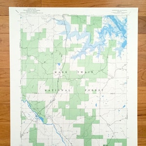 Puede incluir: Un mapa vintage del Bosque Nacional Mark Twain en Misuri. El mapa muestra los límites del bosque, las carreteras, los ríos y los lagos. El mapa está impreso en papel blanco con líneas y texto verdes y azules.