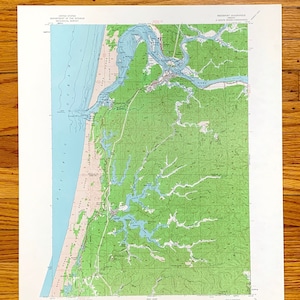 May include: A vintage topographic map of the Reedsport, Oregon area. The map shows the coastline, rivers, and surrounding forest. The map is printed on paper and has a light green and blue color scheme.