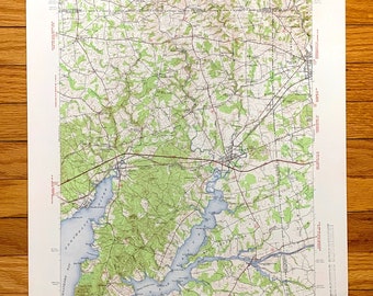 May include: A vintage topographic map showing contour lines, water features, and roads. Printed on white paper, the map is set against a wooden surface. Text indicates the map's title and scale. The map uses imperial units for distance.
