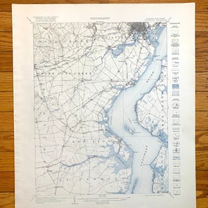 May include: A vintage map of Delaware, New Jersey, showing the topography of the area. The map is printed in black and white with blue accents. The map shows the Delaware River, the White Clay Creek, and the Christina River. The map also shows the towns of Wilmington, Delaware, and New Castle, Delaware.