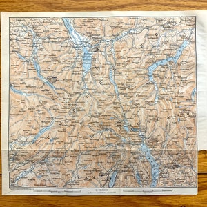 May include: An antique map of the Lake District in England, printed on paper with a light brown background. The map shows the location of lakes, rivers, mountains, and towns. The map is titled "The Lake District" and has a scale of 1:253,440. The map is in good condition, with some minor wear and tear.