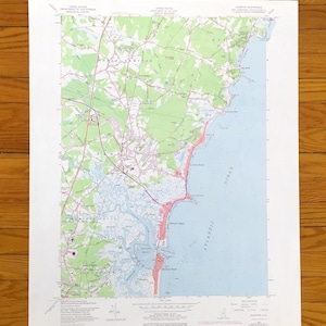Puede incluir: Un mapa topográfico detallado de una región costera, con áreas terrestres verdes y blancas, un océano azul y áreas resaltadas en rojo. El mapa incluye nombres de lugares y curvas de nivel, con el título "HAMPTON QUADRANGLE".