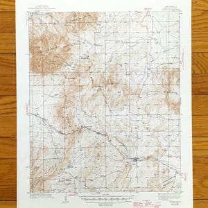 Peut inclure: Une carte topographique vintage avec un motif de grille détaillé, présentant des courbes de niveau et des noms de lieux dans des tons bruns et beiges. La carte est imprimée sur du papier vieilli, blanc cassé, suggérant son importance historique. La carte est une représentation détaillée d'une zone géographique.