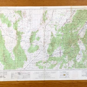 May include: A detailed topographic map titled "Richfield" with green shaded areas representing mountainous terrain. The map features a network of roads, trails, and contour lines, printed on a white paper. The map is folded and lies on a wooden surface.