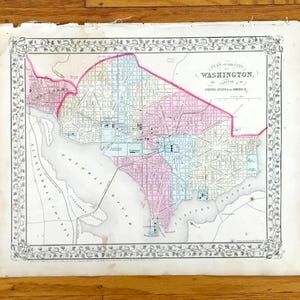 Puede incluir: Mapa antiguo de Washington, D.C., con un borde decorativo. El mapa presenta un diseño detallado de la ciudad, incluyendo calles, el río Potomac y áreas circundantes. El mapa está coloreado en tonos de rosa, azul y verde.