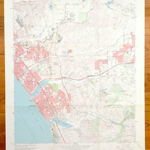 Puede incluir: Un mapa topográfico vintage del Cuadrángulo de San Luis Rey en California. El mapa muestra el área alrededor de la ciudad de Carlsbad, con detalles de carreteras, ríos y elevación. El mapa está impreso en papel y tiene un color marrón claro.