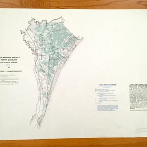 May include: A black and white map of New Hanover County, North Carolina, showing existing conditions. The map is divided into sections with different colors and patterns representing different land uses, such as natural resource management areas, urban areas, and agricultural areas. The map also includes a legend explaining the different symbols and colors used.