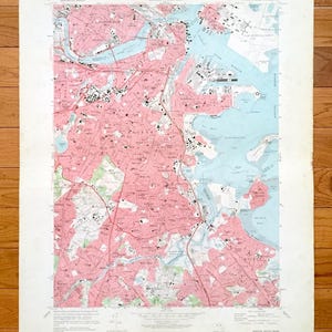 May include: A vintage topographical map of Boston, Massachusetts, showing pink and white land areas, blue water bodies, and black roads. The map is printed on aged paper, showing signs of wear.