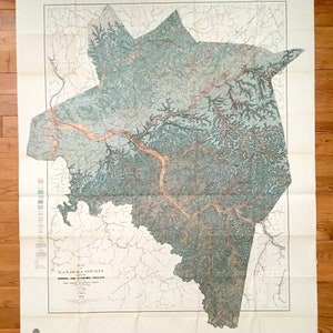 Puede incluir: Un mapa vintage del condado de Kanawha, Virginia Occidental, que muestra la geología general y económica. El mapa está impreso en papel y tiene un fondo marrón claro con líneas verdes y marrones que representan el terreno. El mapa está doblado y tiene un borde blanco.