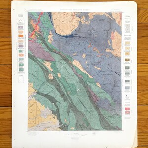 May include: A vintage geological map of California, featuring a detailed illustration with a variety of colors including blue, green, yellow, and pink. The map includes text and a legend, and is printed on aged paper.