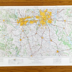 May include: A detailed map of Dallas, Texas, with yellow highlighting the city's urban areas. The map features a network of roads, highways, and green spaces, with the title "DALLAS" at the top. The map is printed on a white paper.