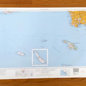 Puede incluir: Un mapa antiguo de Long Beach, California, que muestra el Océano Pacífico y las áreas circundantes. El mapa está impreso en papel blanco e incluye información geográfica detallada, con un enfoque en la costa y las islas. El mapa se muestra sobre una superficie de madera.