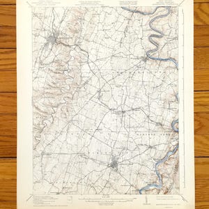 Puede incluir: Un mapa vintage de Harpers Ferry, Virginia Occidental, impreso en blanco y negro con acentos marrones y azules. El mapa muestra la ciudad y sus alrededores, incluidos el río Shenandoah y el río Potomac. El mapa está titulado "Harpers Ferry, W. Va., No. 85".