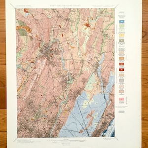 May include: A vintage geological map of the Paterson Quadrangle, New Jersey and New York, showing the surface geology of the area. The map is colour-coded to indicate different types of rock and soil. The map includes a legend explaining the different colours and symbols used.