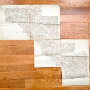 Puede incluir: Un conjunto de cuatro mapas antiguos, impresos en papel blanco, con tinta negra. Los mapas están doblados y muestran una vista topográfica detallada de una región.