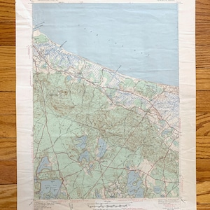 Può includere: Una mappa vintage di Sandwich, Massachusetts, che mostra la costa della baia di Cape Cod, le strade e i laghi. La mappa è intitolata "Sandwich, Mass." e include il testo "Massachusetts Geological Survey, 1:24,000, 7.5 Minute Series".