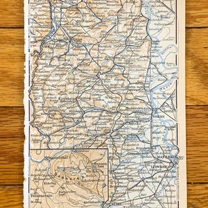 Könnte beinhalten: Eine alte Karte von Deutschland, die den Rhein und die umliegenden Städte und Dörfer zeigt. Die Karte ist in Schwarz, Blau und Braun auf cremefarbenem Papier gedruckt. Die Karte trägt den Titel "Kilometer 1:300.000."