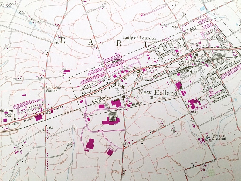 Op de afbeelding: Een zwart-witte kaart van New Holland, Pennsylvania, die de locatie van de Lady of Lourdes Church, een begraafplaats, een pompstation, een rioolwaterzuiveringsinstallatie en een spoorlijn laat zien. De kaart toont ook de locatie van verschillende wegen en straten.