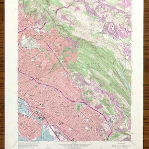 Puede incluir: Un mapa topográfico vintage de Oakland Este, California, que muestra las calles de la ciudad, los parques y las colinas circundantes. El mapa está impreso en papel y tiene un color marrón claro. El mapa se titula "Oakland East Quadrangle" e incluye el texto "15 Minute Series Topographic".