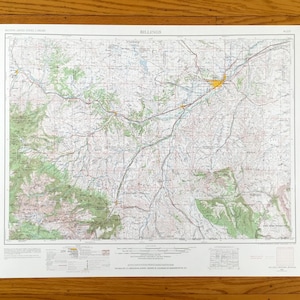 Könnte beinhalten: Eine detaillierte topografische Karte von Billings, Montana, mit einem Netzwerk von Straßen, Flüssen und Höhenlinien. Die Karte ist auf weißem Papier gedruckt und enthält oben den Text "Billings". Die Karte befindet sich vor einem Holzgrund.
