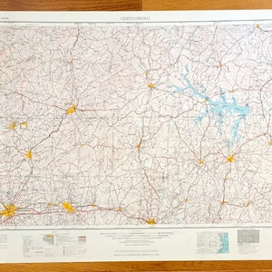 May include: A vintage map of Greensboro, North Carolina, showing roads, highways, and towns. The map is printed on a white background with red and black lines. The map is titled "Greensboro" in the top left corner.