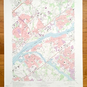 May include: A vintage map of the area around Philadelphia, Pennsylvania, focusing on the Delaware River. The map shows the river winding through the landscape, with various towns and cities marked along its banks. The map is printed in black and white, with some areas shaded in pink and blue. The map is titled "Riverton, N.J."