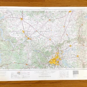 May include: A detailed map of Nashville, Tennessee, featuring roads, rivers, and green-shaded areas. The map has a white border and is printed on paper. The city center is highlighted in yellow.