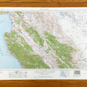 May include: A vintage topographic map of Santa Cruz, California, showing the coastline, mountains, and roads. The map is printed on white paper with blue, green, and brown lines and text. The map is titled "SANTA CRUZ" in the upper center.