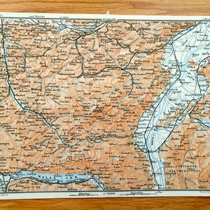 Puede incluir: Un mapa vintage de los Alpes suizos, que presenta una topografía detallada, ríos y lagos. El mapa está impreso en tonos marrones, azules y verdes, con líneas negras para las carreteras y las fronteras. El mapa incluye los nombres de las ciudades y las montañas, así como los nombres de los lagos Walensee y Vierwaldstättersee.