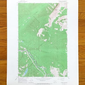 Peut inclure: Une carte topographique de la région du lac Stanton, avec des reliefs ombrés verts et blancs. La carte montre les courbes de niveau, les cours d'eau et les noms de lieux. La carte est imprimée sur papier blanc.