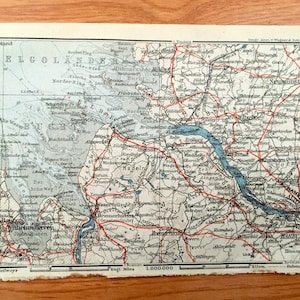 May include: An antique map of Helgoland, Germany, with red and blue lines indicating roads and waterways. The map is printed on cream-colored paper and includes the text "Helgoland" and "Helgolander" in large, bold letters.
