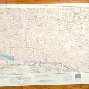 Puede incluir: Un mapa vintage de North Platte, Nebraska, con un fondo marrón claro y marcas azules y verdes. El mapa muestra carreteras, ríos y otras características geográficas. El título "NORTH PLATTE" está impreso en la parte superior central del mapa.