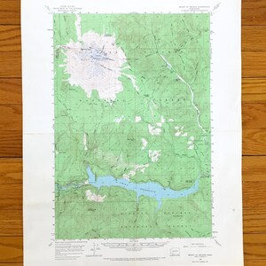 May include: A United States Geological Survey topographic map of the Mount St. Helens quadrangle in Washington. The map features green terrain, white glacial areas, and a blue reservoir, with detailed contour lines and grid coordinates throughout.