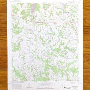 May include: A vintage topographic map of Mount William, Massachusetts, featuring detailed contour lines, roads, and forested areas. The map is printed on white paper and includes text indicating the map's origin and scale. The map is displayed on a wooden surface.